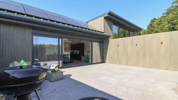 A modern house with a patio, a barbecue grill, and a large window.