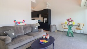 A modern living room with a grey sofa, a coffee table, and a dining area with a glass table and chairs.