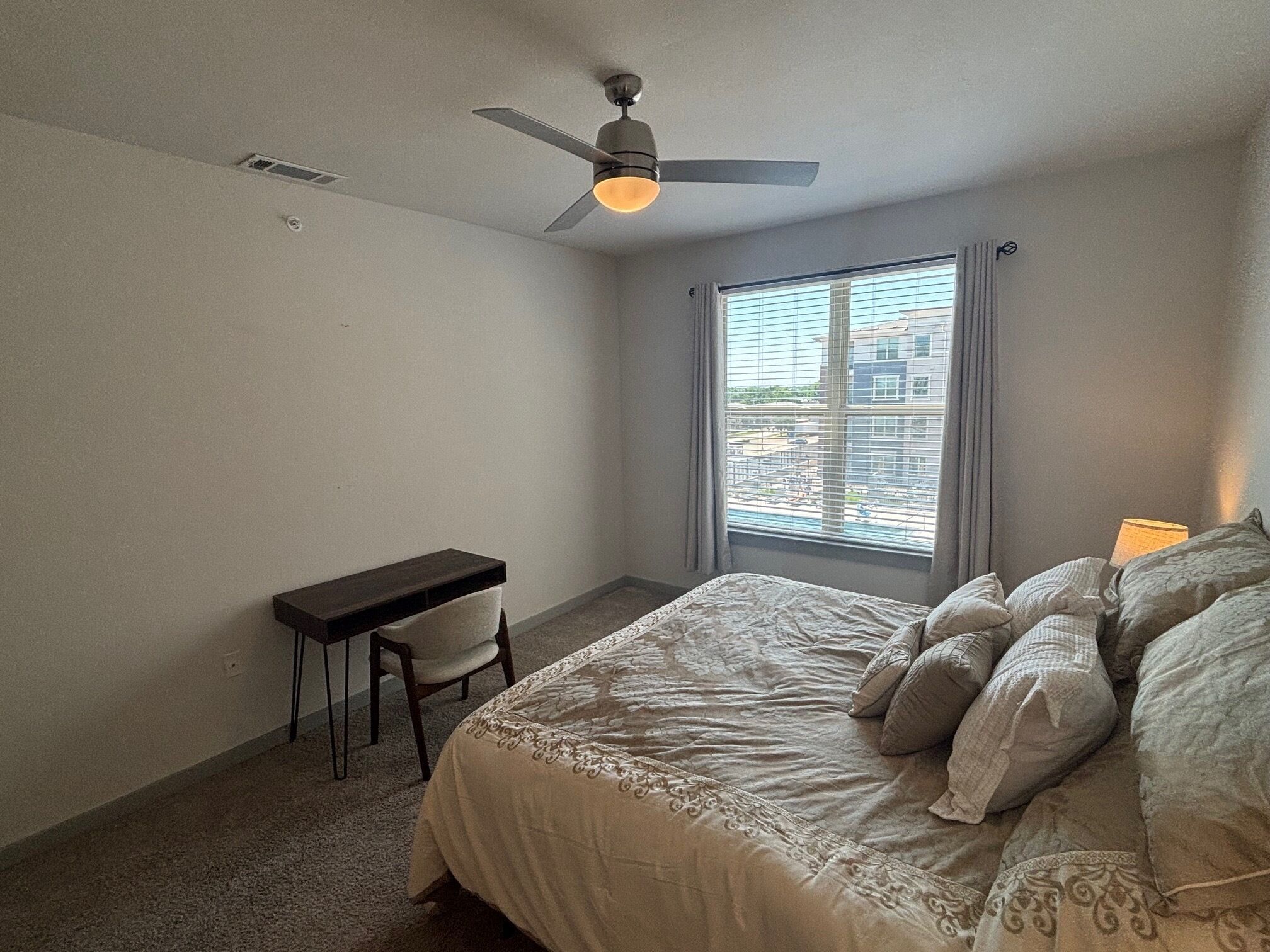 A bedroom with a bed, a desk, and a ceiling fan.