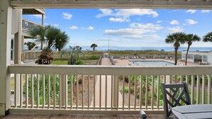 Un balcon avec vue sur une piscine, des palmiers et une plage.