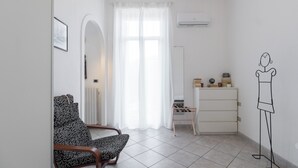 Une pièce au décor minimaliste, avec un fauteuil à motifs, une commode, un radiateur et un climatiseur fixé au mur.