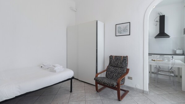 A minimalist room with a bed, a chair, a wardrobe, and a small table with a book and mug.