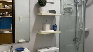 A bathroom with a sink, toilet, and shower. There are shelves above the toilet with toiletries and a small plant. - Casa Z - Bali Oasis Phase 2 (Pasig)
