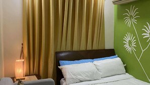 A hotel room with a bed, a nightstand with a lamp, and a green wall with floral patterns. - Casa Z - Bali Oasis Phase 2 (Pasig)