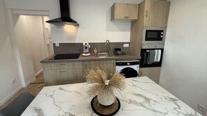 A compact kitchen with a sink, stove, microwave, and dishwasher. There's a marble table with a decorative vase. - Apartment in Ecommoy Near Le Mans Circuit (Ecommoy)