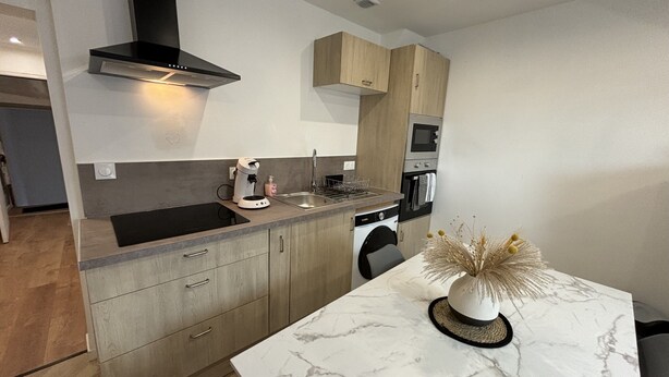 A modern kitchen with a marble countertop, built-in appliances, and wooden cabinets. - Apartment in Ecommoy Near Le Mans Circuit (Ecommoy)