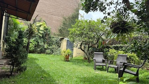 A lush garden with a grassy lawn, a wooden pergola, and a seating area with chairs.