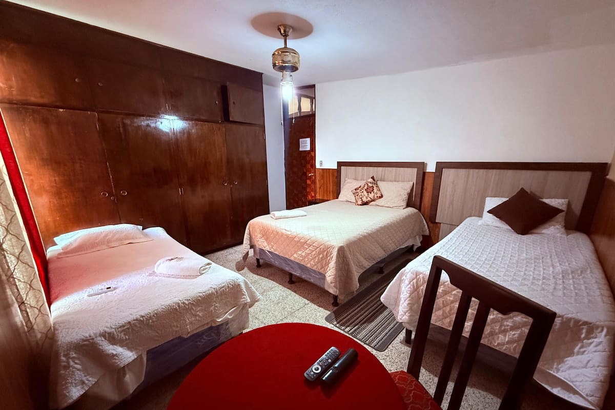Een hotelkamer met drie bedden, een rode tafel en een plafondventilator.