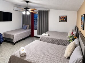 A hotel room with two beds, a ceiling fan, an air conditioning unit, a TV, and a painting on the wall. - EL TEJAR HOSTAL  (Guatemala City)
