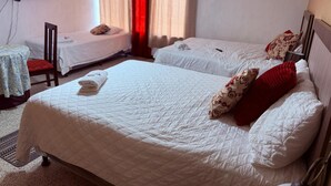 A hotel room with two single beds, a small table with a chair, and a TV mounted on the wall.