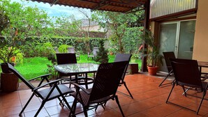 A patio with a glass table and chairs, surrounded by potted plants and a green garden.