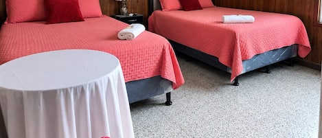 A hotel room with two beds, a round table, a painting on the wall, and an air conditioning unit.