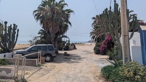A gravel path leading to a beach with a parked car and a palm tree. - Beachfront Studios for couples, digital nomads, and surfers  in Tamraght, Aourir (awrir)