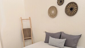 A neatly made bed with a dark blanket and pillows, a small wooden ladder, and decorative wall hangings. - Beachfront Studios for couples, digital nomads, and surfers  in Tamraght, Aourir (awrir)