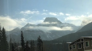 A mountain cabin with a view of snow-capped peaks and a forested valley.