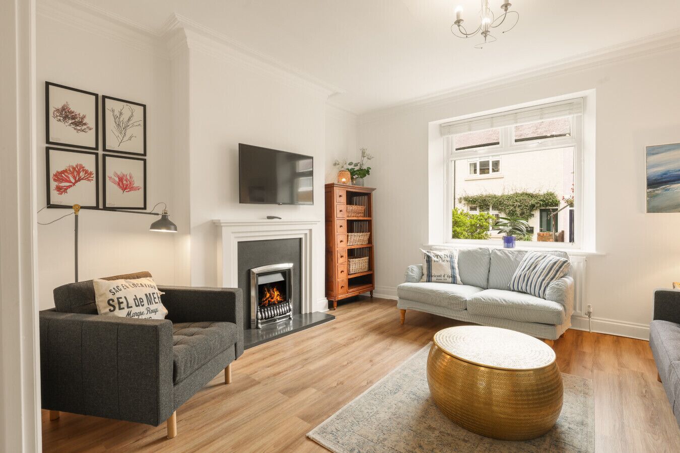 A modern living room with a fireplace, a sofa, a TV, and a window with a view of greenery.