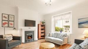 Een woonkamer met een open haard, een televisie en een groot raam met uitzicht op gebouwen.