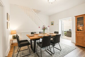 A dining area with a wooden table set for four, black chairs, a chandelier, and a view of the outside. - No.20 - North East Escapes (Amble)