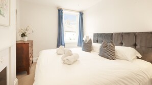 Een keurig opgeruimde slaapkamer met een groot bed, een dressoir en een raam met gordijnen.