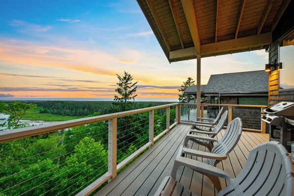 Une terrasse en bois avec coin salon extérieur et espace barbecue, offrant une vue sur un paysage boisé.