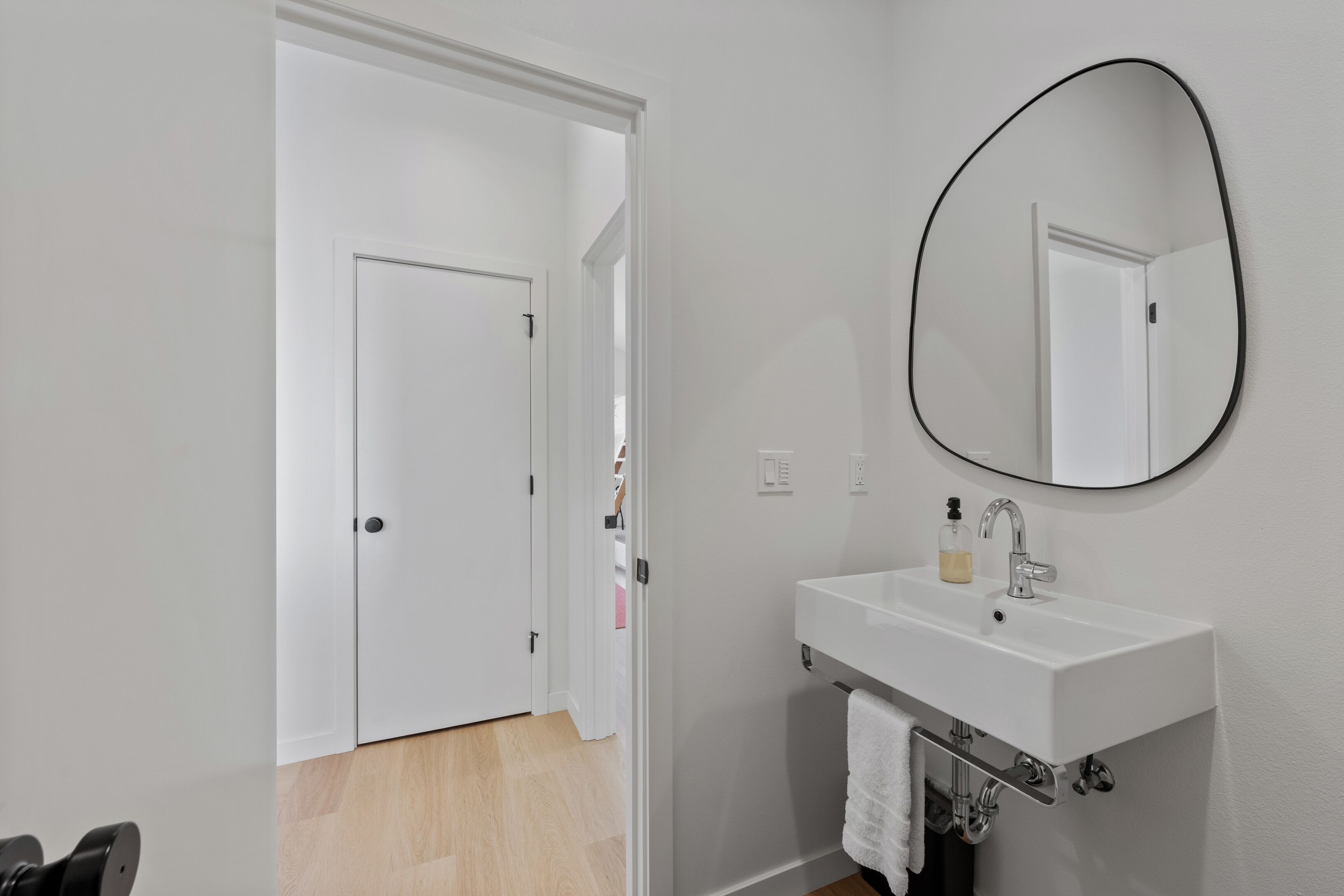 A bathroom with a white sink, a mirror, and a door leading to another room.