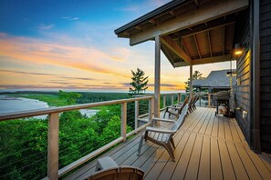 Une terrasse en bois, dotée de chaises, qui offre une vue sur une étendue d’eau et sur la verdure environnante.