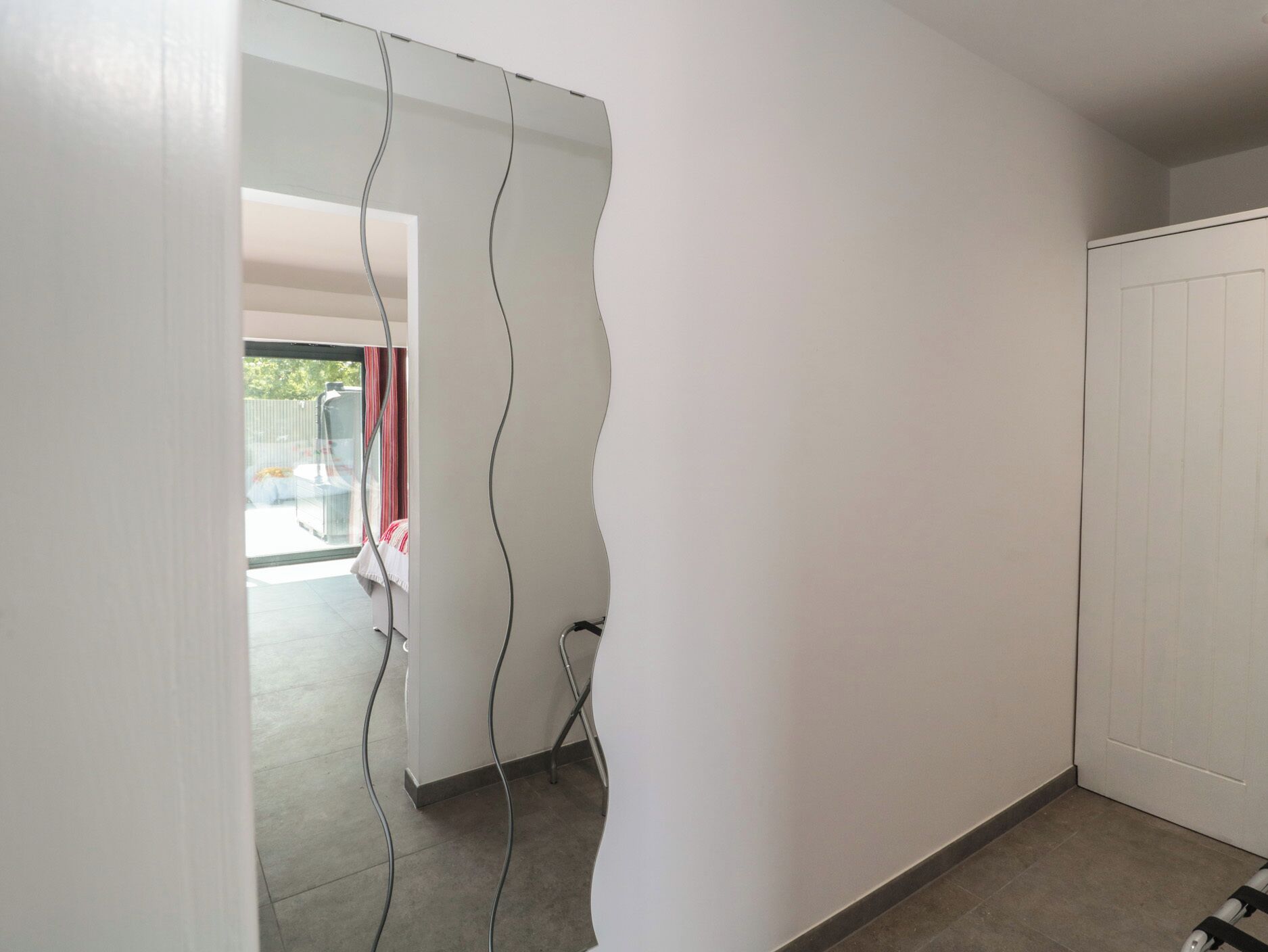 Un pasillo con una puerta blanca, una puerta de cristal que da a un área exterior y un suelo de baldosas.