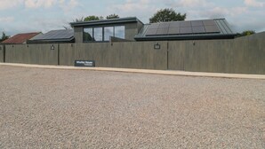 A building with a metal fence, solar panels on the roof, and a gravel driveway. - Noflash Malpal (Bristol)