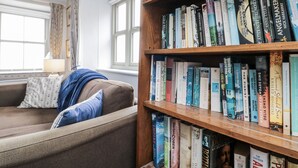 A cozy reading nook with a wooden bookshelf filled with books, a patterned cushion, and a lamp on a side table. - Shelstone (Whitby)