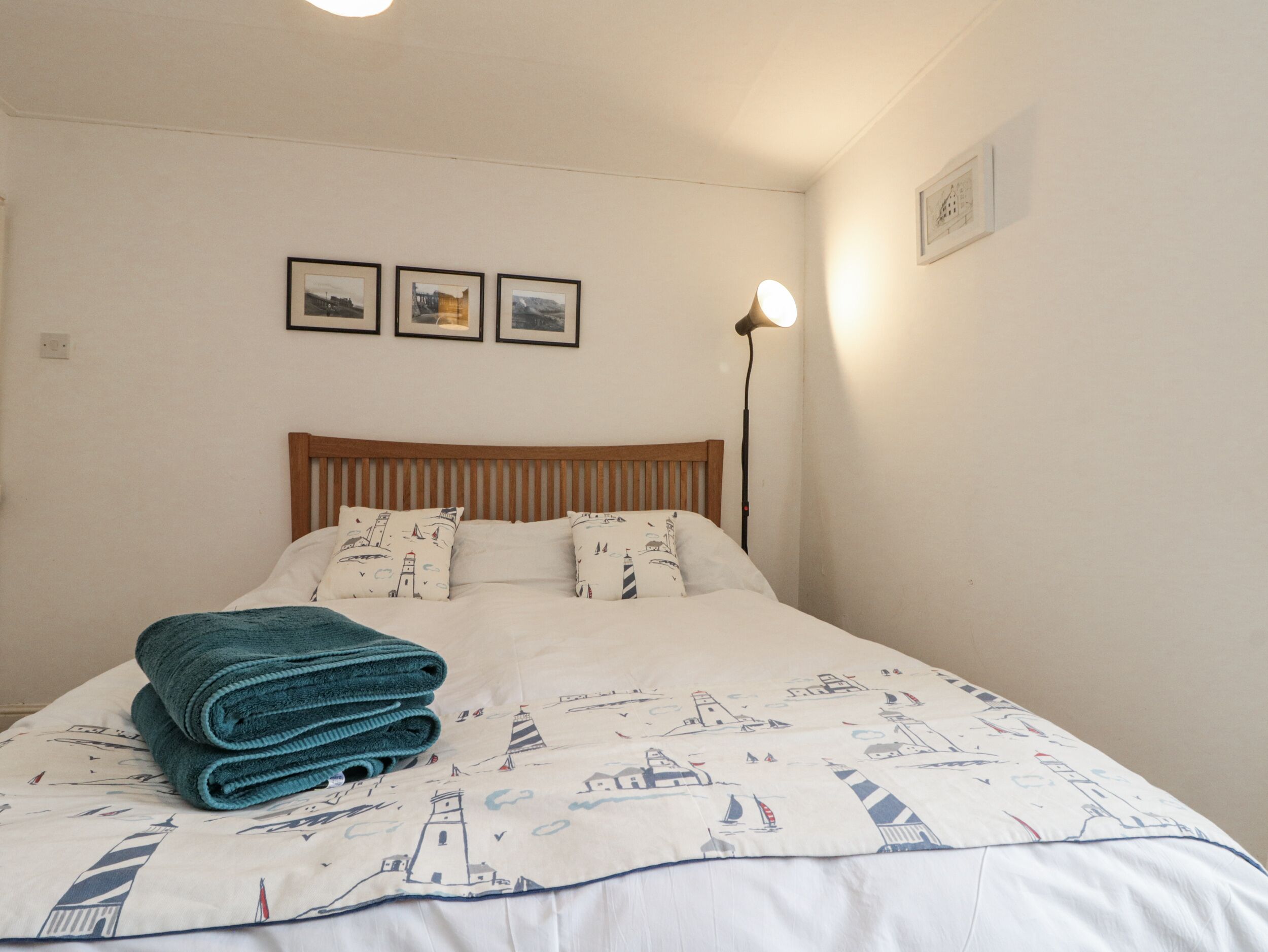 A neatly made bed with a patterned duvet cover, a stack of folded towels, and a bedside lamp.