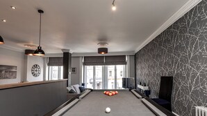 Uma mesa de bilhar numa sala moderna com vista para a cidade, um relógio e um espaço de bar.