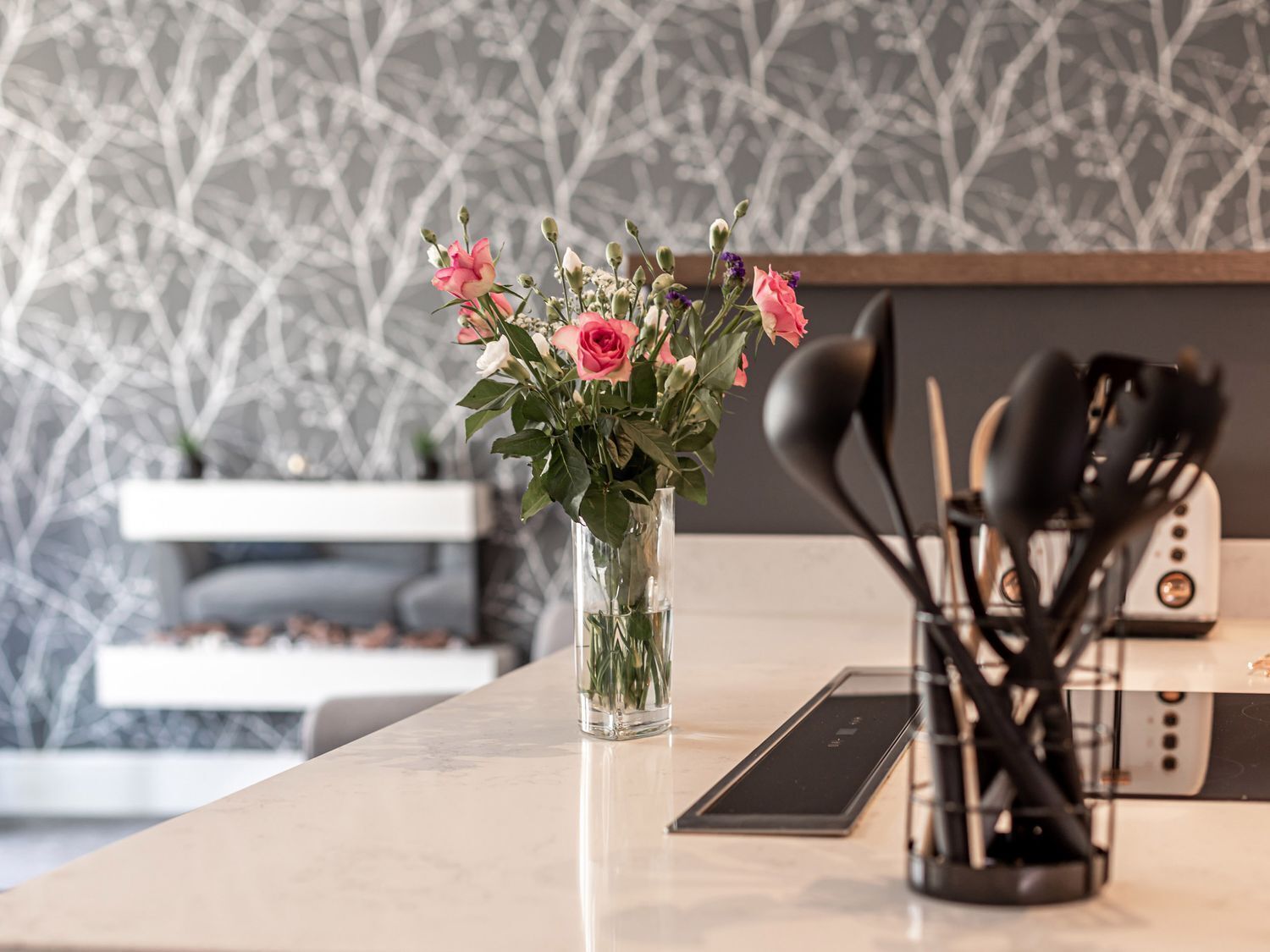 A kitchen with a marble countertop, a vase with pink flowers, and a modern toaster.