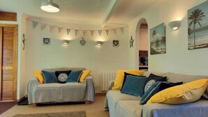 Una sala de estar acogedora con dos sofás, un tapiz decorativo y un cuadro con motivos playeros.