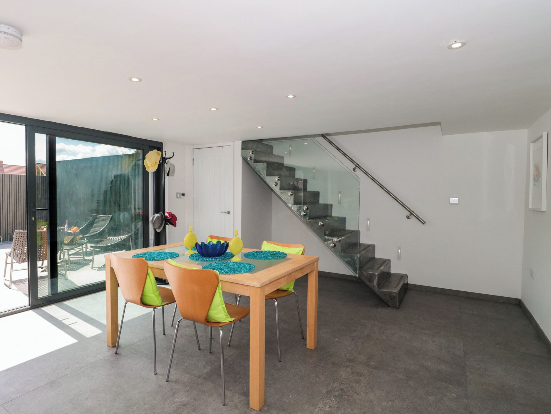 A modern dining area with a glass table, chairs, and a staircase.