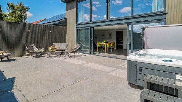 Une maison moderne dotée d’un patio comprenant un jacuzzi, un espace salon extérieur et une porte vitrée donnant sur une salle à manger intérieure.