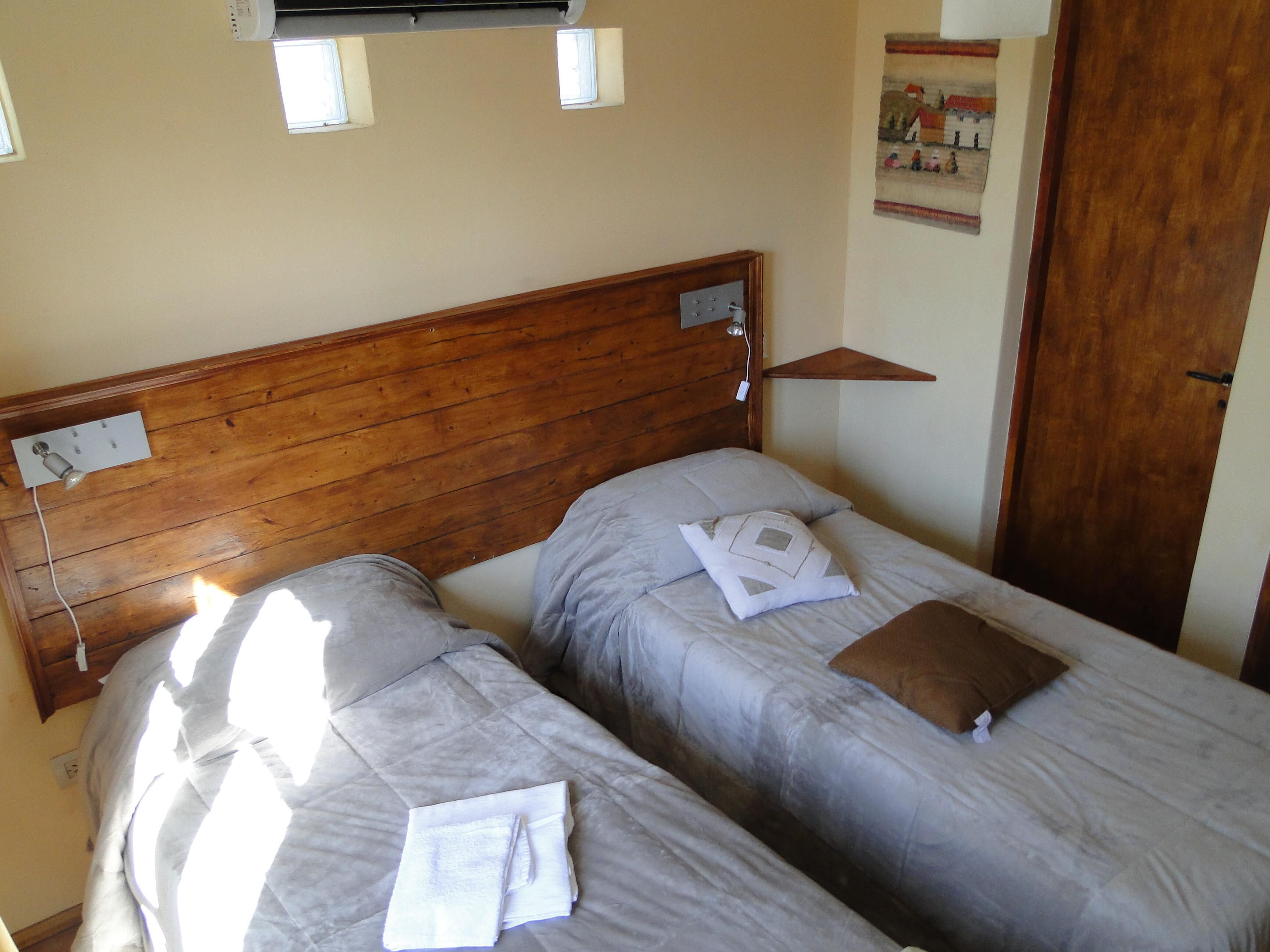 A room with two beds, wooden headboards, a small table, and a door.