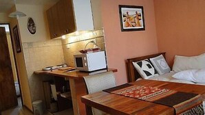 Una habitación pequeña con kitchenette, una cama con ropa blanca y una pequeña mesa de comedor.