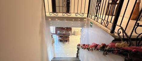 A staircase with a railing decorated with festive garlands, leading to a room with a dining table and chairs.