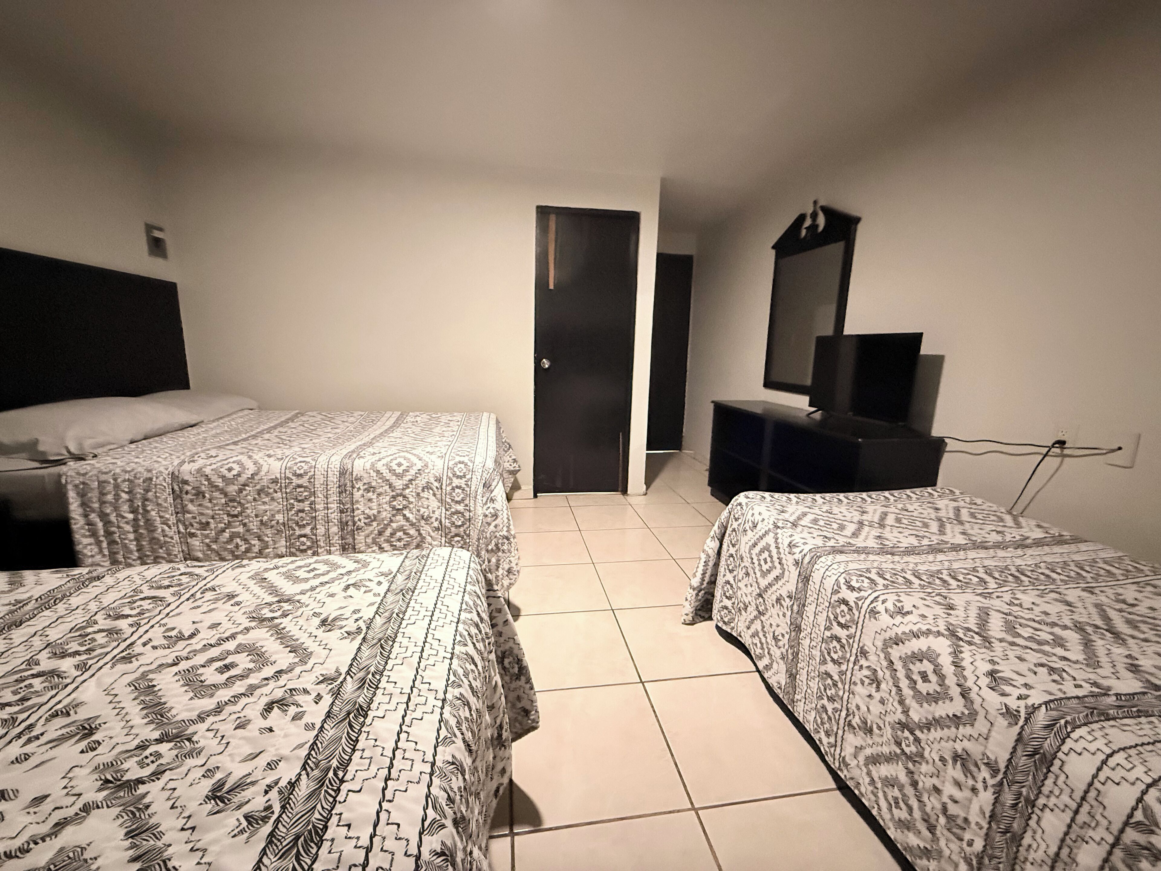 A room with two beds, a TV on a stand, and a door leading to another room.