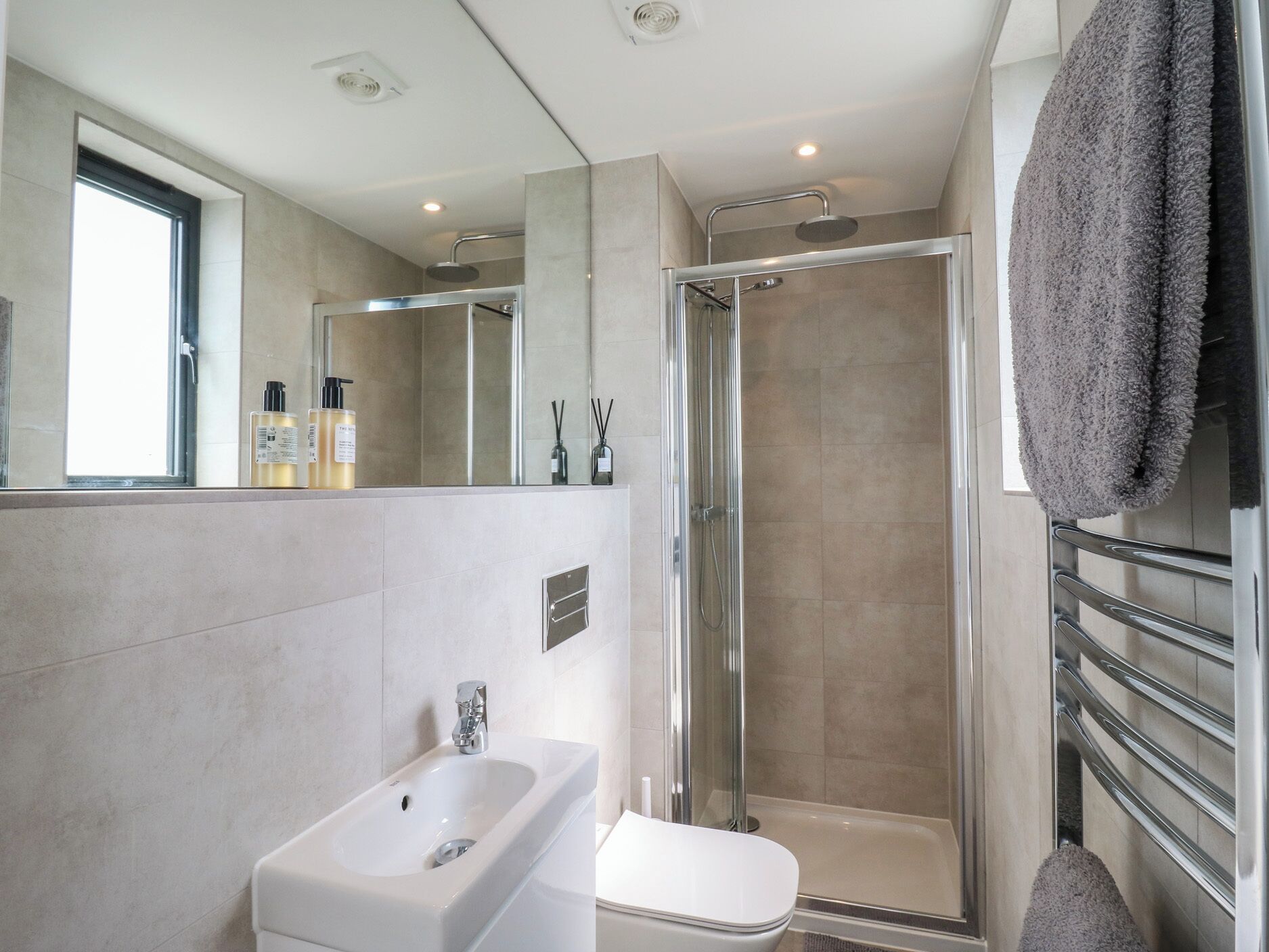 A modern bathroom with a glass-enclosed shower, a white sink, and a large mirror.