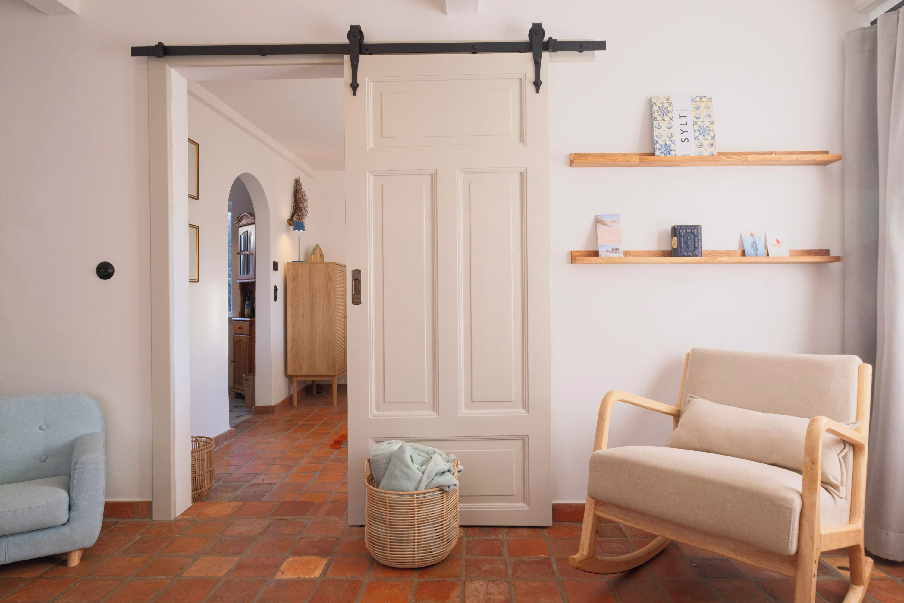 A room with a sliding door, a sofa, a chair, a basket, and shelves with books and decorative items.