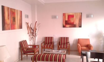 Una sala de estar con sillones a rayas, un sofá y una mesa de centro. Hay cuadros abstractos en las paredes y un jarrón con plantas secas.