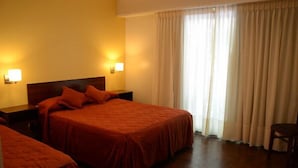 Ein Hotelzimmer mit zwei Betten, einem Holzkopfteil, Nachttischlampen und Blick durch ein mit Vorhängen versehenes Fenster nach draußen.
