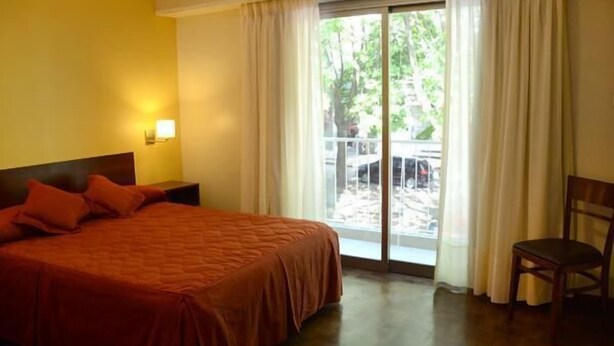 Ein Hotelzimmer mit Bett, Stuhl, einem Fenster mit Vorhängen und Blick ins Freie.