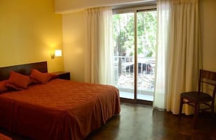 Habitación de hotel con cama, una silla, ventana con cortinas y vistas al exterior.
