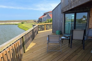 A wooden deck with a view of the water, a chair, a small table, and a building with a red roof in the background.