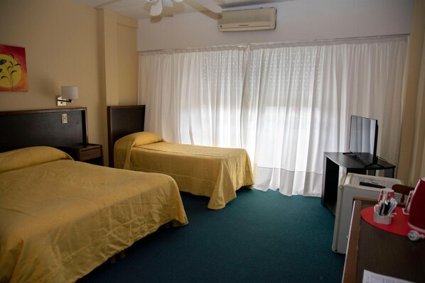 Une chambre d’hôtel avec deux lits, un bureau avec un ordinateur, une télévision et une fenêtre avec des rideaux légers.