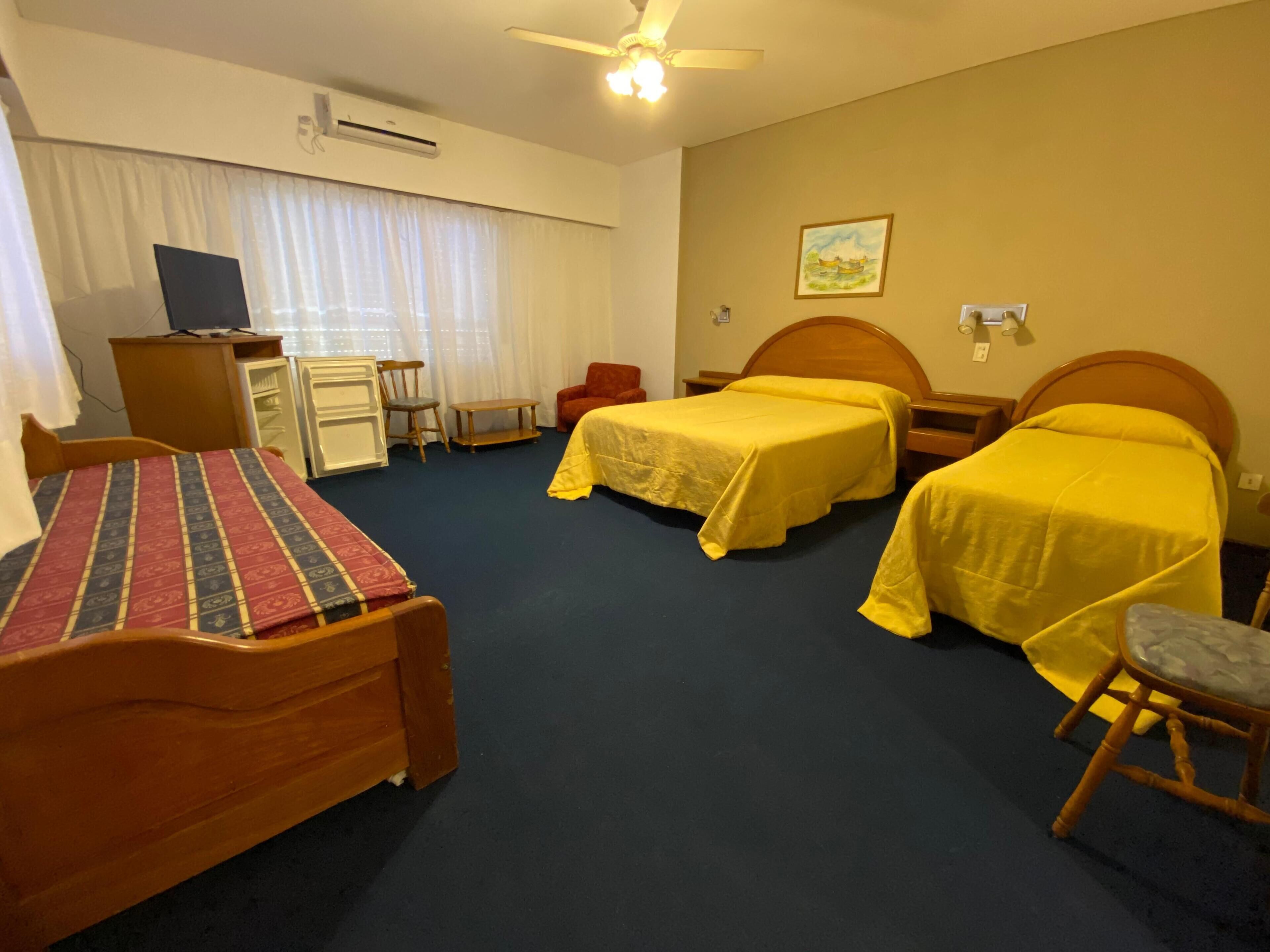 A hotel room with two beds, a desk, a chair, a small table, and a ceiling fan.