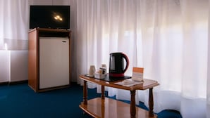 Una camera d'albergo con una scrivania in legno, una macchina per caffè, un telecomando e una televisione su un mobile.
