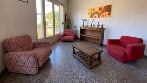 Un soggiorno con un divano rosso a motivi, un tavolino in legno e una poltrona rossa. Si nota un mobile in legno con oggetti decorativi e un quadro appeso al muro.